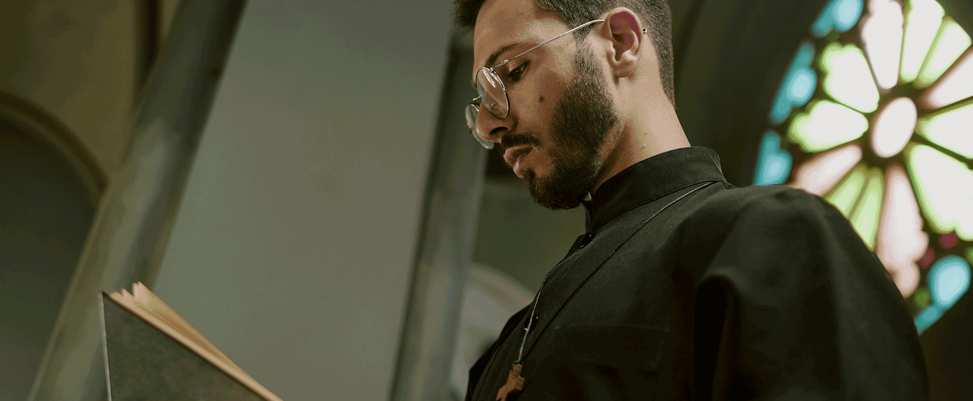 A pastor and biblical theology student of Aidan University studying in a church with a stained glass pastel rose window in the background.